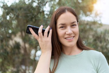 Genç ve güzel bir kadın gülümsüyor. Parktaki akıllı telefondan kendine güvenen bir sesli mesaj dinliyor.