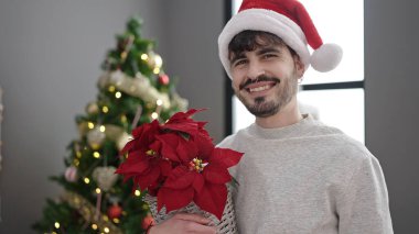 Genç İspanyol adam Noel bitkisini evde tutuyor.