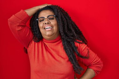 Artı, kırmızı arka planda dikilen, kendine güvenen, el hareketleriyle saçlarına dokunan çekici ve şık pozlar veren İspanyol kadın. 