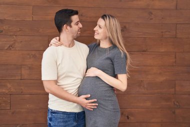 Erkek ve kadın çift, izole edilmiş ahşap arka planda bebek beklerken birbirlerine sarılıyorlar.