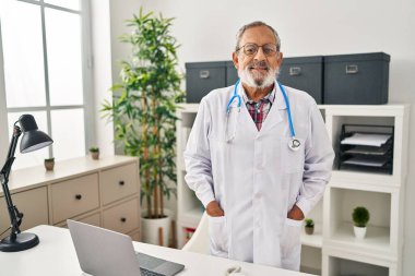 Senior grey-haired man doctor smiling confident standing at clinic