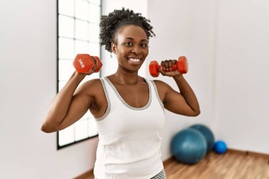 Spor merkezinde dambılları kullanarak gülümseyen Afrikalı Amerikalı kadın.