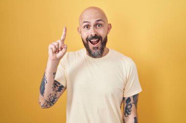 Sarı arka planda duran İspanyol dövmeli adam başarılı bir fikir işaret ediyor. Heyecanlı ve mutlu. Bir numara.. 