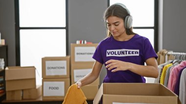 İlham verici genç İspanyol kadın gönüllü, fevkalade ayakta, müziğe dalmış, bir sosyal merkezde yardım için kıyafet topluyor, özgeciliğiyle birlik ve sosyal desteği somutlaştırıyor..