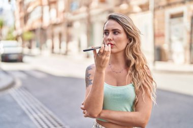 Young blonde woman talking on smartphone with serious expression at street