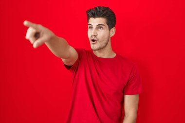 Genç İspanyol adam kırmızı arka planda dikiliyor. Parmağı önde, ağzı açık, şaşırmış bir ifade. Önde bir şey var. 