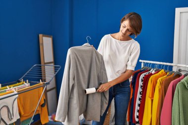 Genç, güzel, İspanyol bir kadın gülümsüyor. Çamaşır odasında kendine güvenen bir temizlikçi ceketi kullanıyor.