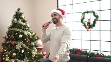 Genç İspanyol adam Noel ağacının yanında şarkı söylüyor.