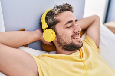 Young man listening to music lying on bed at bedroom