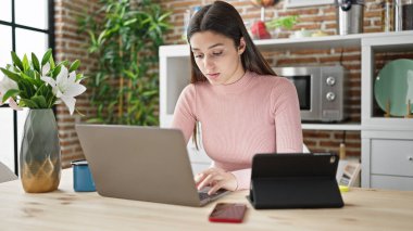 Genç ve güzel İspanyol kadın yemek odasındaki masada dizüstü bilgisayar ve dokunmatik ped kullanıyor.