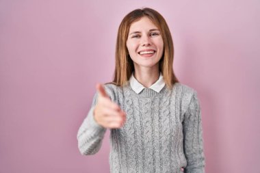 Pembe arka planda duran güzel bir kadın gülümseyerek selamlama ve hoş geldin demek için tokalaşıyor. başarılı iş. 