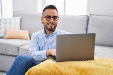 Genç İspanyol adam evde dizüstü bilgisayar kullanıyor.