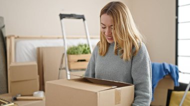 Genç sarışın kadın yeni evinde kendine güvenen bir paket tutuyor.