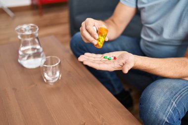 Orta yaşlı bir adam evdeki kanepede oturup hap alıyor.