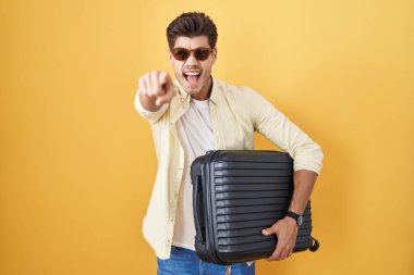 Yaz tatilinde bavulu tutan genç İspanyol adam kameraya kızgın ve sinirli bir şekilde işaret ediyor. 