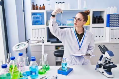Young woman scientist reading document measuring liquid at laboratory