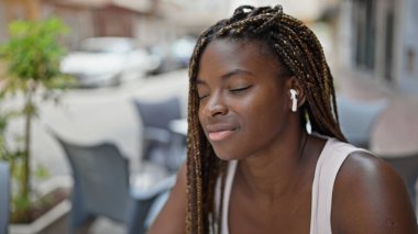 Afro-Amerikalı bir kadın müzik dinlerken kahve dükkanının terasında oturup düşünüyor.