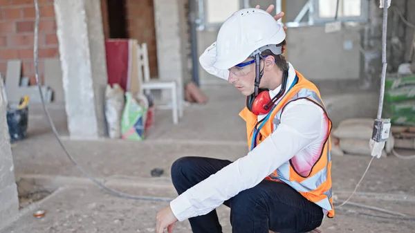 Young caucasian man architect tired sitting on floor at construction site