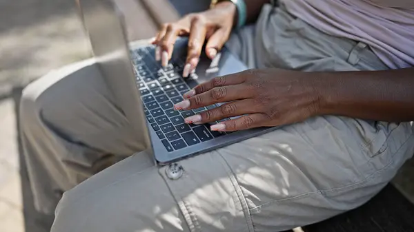 African american woman typing laptop sitting on bench at park