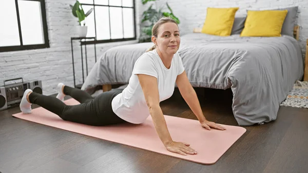 Blissful morning stretch! charming young, blonde woman lying on bedroom floor, smiling while perfecting back stretch pose.