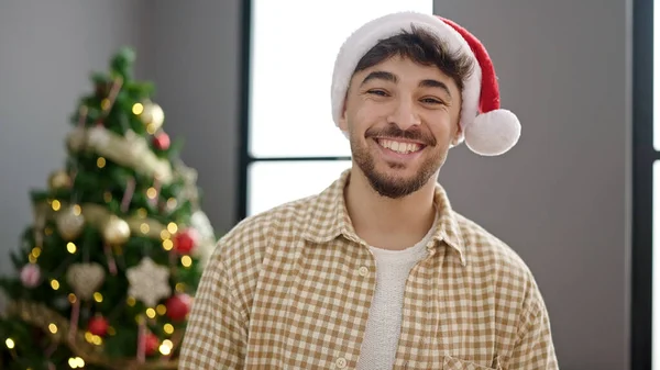 Young arab man smiling confident standing by christmas tree at home