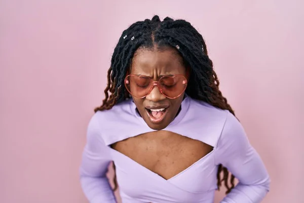 アフリカの女性は 不快感 痛みを伴う病気を感じるため 胃の上にピンクの背景の上に立って編組された髪をしています アチェのコンセプト — ストック写真
