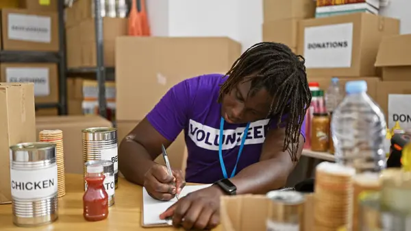 African american man volunteer smiling confident writing on document at charity center