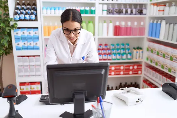 Young arab woman pharmacist smiling confident using computer at pharmacy