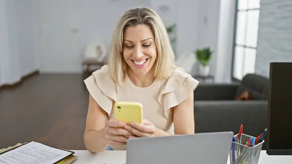 Young blonde woman business worker using laptop and smartphone at the office