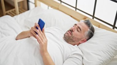 Yatakta telefon kullanan orta yaşlı bir adam.