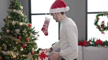 Noel Baba şapkalı genç adam evdeki kanepede oturuyor.