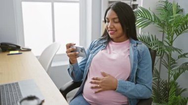Genç hamile iş kadını akıllı telefondan Belly 'e dokunan videolar izliyor.
