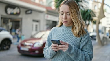 Sokakta akıllı telefon kullanan genç sarışın kadın.