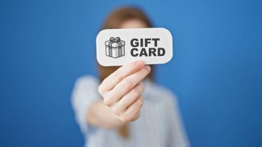 Sarışın genç bir kadın mavi arka planda hediye kartı tutuyor.