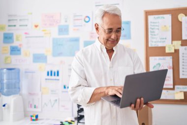 Ofiste çalışırken dizüstü bilgisayar kullanan orta yaşlı, kır saçlı bir iş adamı.