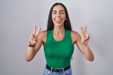 İzole edilmiş arka planda duran genç bir kadın her iki elinde parmaklarını göstererek gülümseyerek zafer işareti yapıyor. İki numara.. 