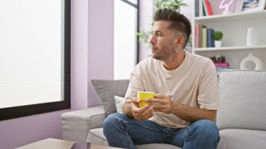 Yakışıklı genç İspanyol adam sabah espresso yudumluyor, evdeki oturma odasındaki kanepede rahatça dinleniyor.