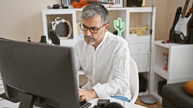 Genç, gri saçlı İspanyol bir radyo stüdyosunda haber sunan mikrofon ve bilgisayar arasında birden fazla iş yapan biri.