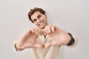 İzole edilmiş arka planda duran genç adam, aşka gülümseyip elleriyle kalp sembolü çiziyor. romantik kavram. 