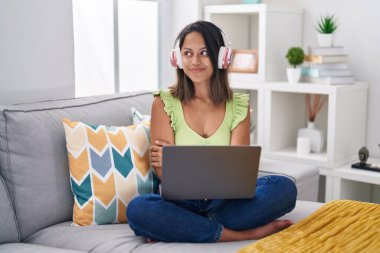 Evde dizüstü bilgisayar kullanan İspanyol genç bir kadın gülümseyip yan tarafa bakıyor ve düşünüyor.. 