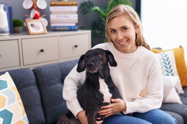 Young blonde woman hugging dog sitting on sofa at home