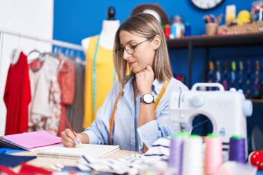 Young beautiful hispanic woman tailor smiling confident drawing on notebook at clothing factory