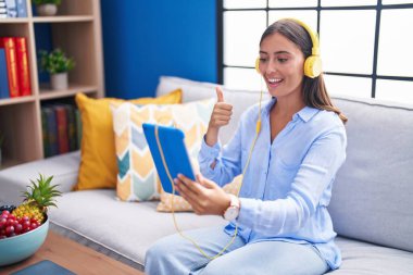 Genç İspanyol kadın tabletle video görüşmesi yapıyor, kulaklık takıyor, gülümsüyor, gülümsüyor ve olumlu bakıyor. 