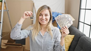 Yeni evinde elinde dolar ve anahtar tutan genç sarışın kadın.