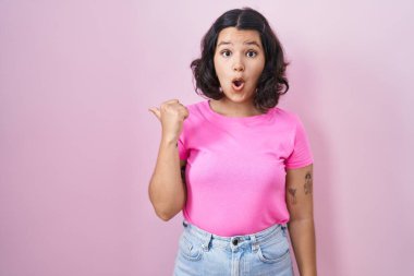 Pembe arka planda duran genç İspanyol kadın elleri yana doğru işaret ederek şaşırdı, ağzı açık hayret içinde kaldı.. 