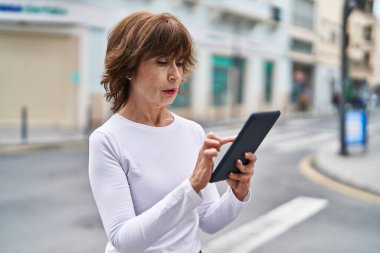 Orta yaşlı bir kadın sokakta ciddi bir ifadeyle dokunmatik ped kullanıyor.
