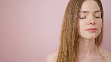 Genç sarışın kadın pembe arka planda kapalı gözlerle nefes alıyor.