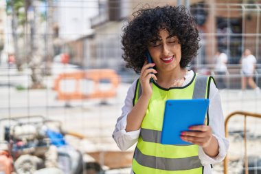 Young middle east woman architect talking on smartphone using touchpad at street