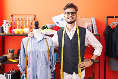 Genç İspanyol terzi gülümsüyor Atölyede kendine güvenen manikine yaslanıyor