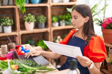 Çiçekçide dizüstü bilgisayar kullanarak kitap okuyan güzel İspanyol bir çiçekçi kadın.